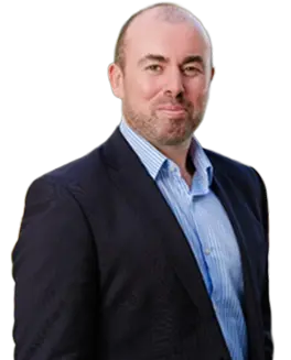 A man with short hair and a beard, representing Duffy Capital, is wearing a dark suit jacket over a light blue dress shirt, standing and smiling slightly at the camera.