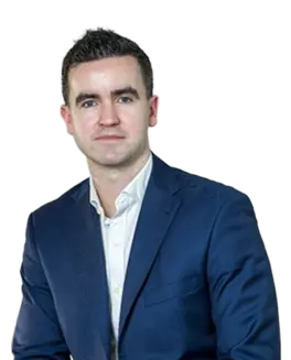 A man with short dark hair, wearing a white shirt and a dark blue suit jacket, poses in front of a plain background, representing Duffy Capital.